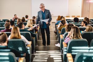 Happy senior professor talking to his students while collecting evaluations in lecture hall.