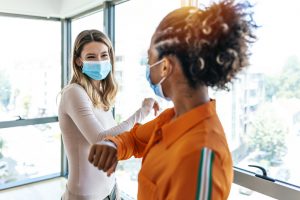 Two colleagues in medical masks avoiding  handshake when meeting in the office, greeting with bumping elbows during corona virus COVID-19 epidemic in office, Social distancing concept