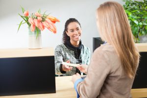 A Caucasian woman bank customer making a transaction with a bank teller in a retail bank. The teller is a young black woman, an African American professional working with her computer terminal and serving the customer with the transaction. Photographed from behind the shoulder of the customer in a horizontal format.